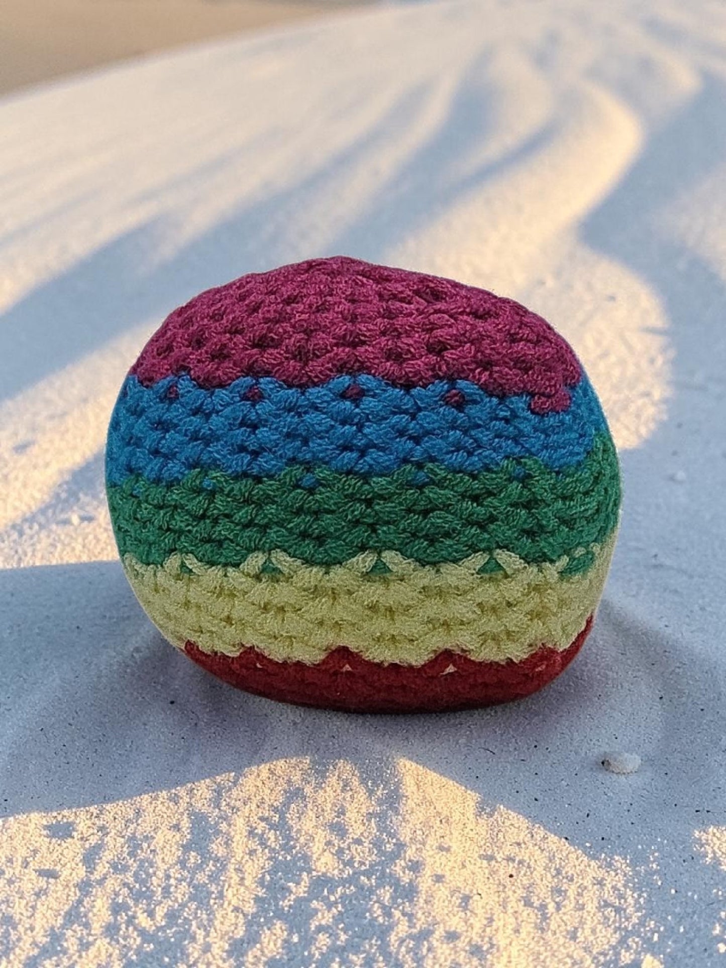 Colorful crocheted ball on a sandy surface