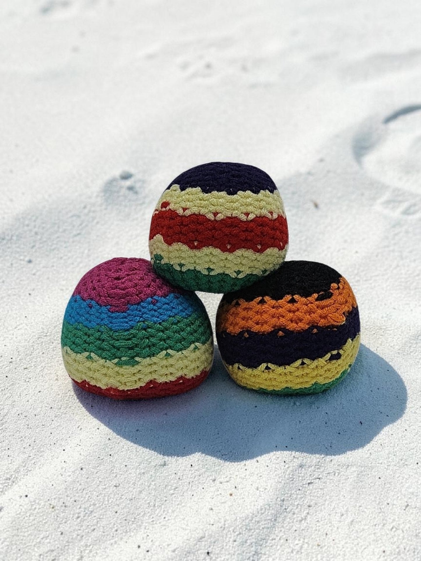 Three colorful crocheted balls on a sandy surface
