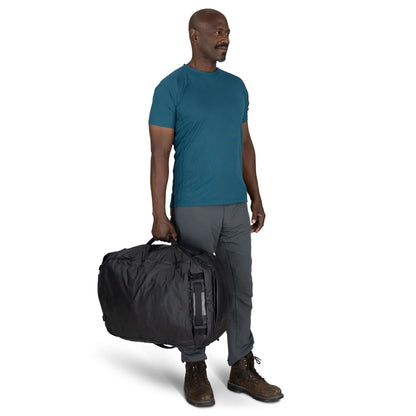 On-Body Side Carry (Front View) – Male model carrying the Osprey Transporter Duffel 65 in Raven Black by hand for scale.